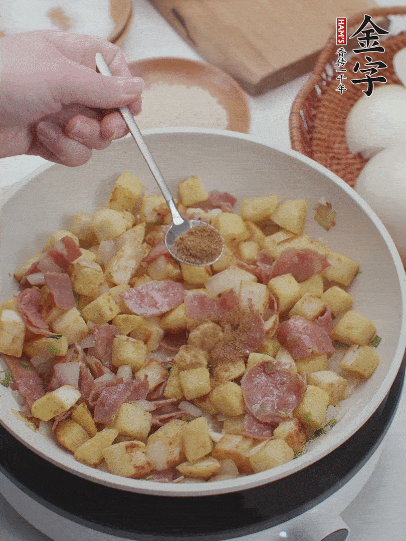 起鍋少油，煸香洋蔥丁、蔥白，加入金字培根火腿翻炒幾下，再加入饅頭丁、1小勺孜然粉、少許鹽翻炒均勻并鋪平。